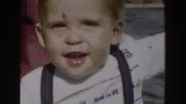 Glendale California (1962): Toddler Wearing Blue Overalls Walks To Green Shrub On