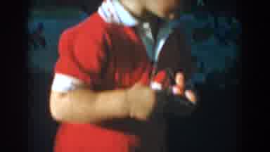 Glendale California (1962): Boy In Red Oneness Stands Picking Up Toy In Backyard