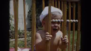 GLENDALE CALIFORNIA-1962: Infant Wearing White Hat Looks Through Brown Wooden Playpen