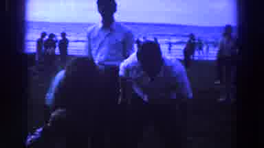 Ireland (1961): Man Wearing White Shirt Stands On Beach Holding Black Object