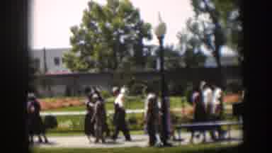 Wyoming (1951): People Walking Past Blooming Orange Flowers On A Clear Day
