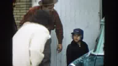 Michigan (1957): Woman Wearing White Coat Gives Small Boy Wearing Blue Hat Kiss on