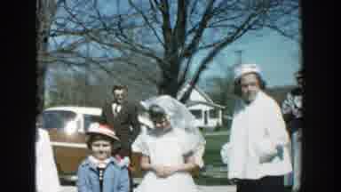 Michigan (1957): Four People Standing Near Brown Car On A Bright Sunny Day