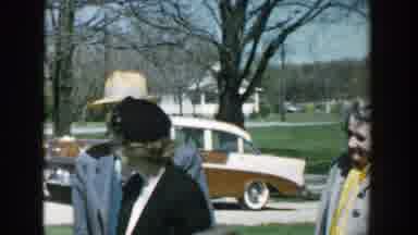 Michigan (1957): Group Of People Stand Near Green Car On A Bright Sunny Day