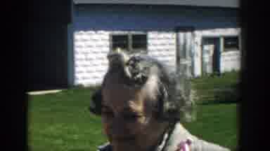 Michigan (1957): Two Women Stand Near White Shed And Green Car On A Sunny Day