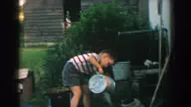 Michigan (1957): Man Picks Weeds From Farmland While Boy Waters Flowers