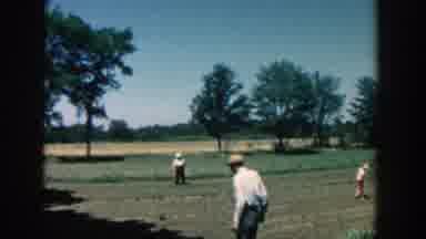 Michigan (1957): Man Wearing White Hat Picks Items From Farm Field On A Sunny Day