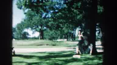 Michigan (1957): Boy Wearing Black Pants Stands Against Large Tree On A Sunny Day