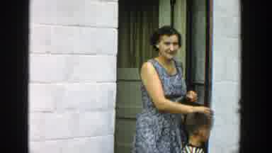 Michigan (1957): Woman Wearing Blue Dress Walks Out Of A White House On A Clear