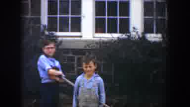 Cuba (1951): Two Boys Wearing Blue Shirts Stand Near Grey Stone And White House On