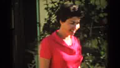 North Hollywood California (1962): Smiling Lady Walks Outside To Pick Something Up