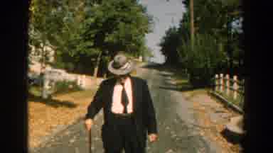 Michigan (1959): Man Wearing Black Suit And Grey Hat Walks Down Street With Brown