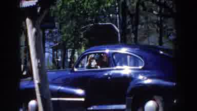 Michigan (1959): Two People Wave From A Car Window Parked Outside Near Trees
