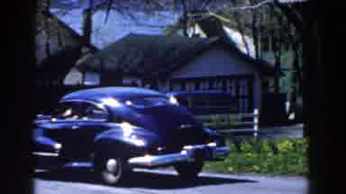 Michigan (1959): Black Car Enters Driveway Of A White House On A Sunny Day