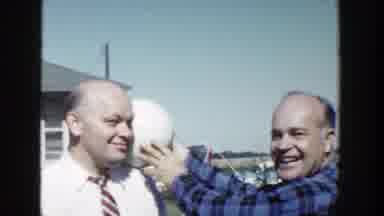 Wisconsin (1958): Man Wearing Blue Shirt Holds White Ball Next To Head Of Man