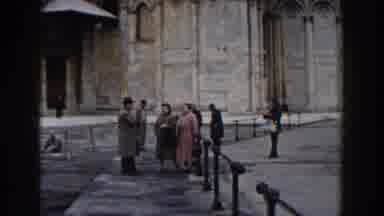 Pisa Italy (1959): Small Group Of People Looking At Tan Building On A Clear Day