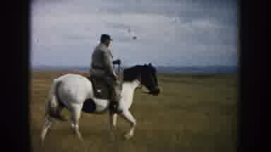South Dakota (1953): Man Wearing Black Hat Rides Black And White Horse Across Tan