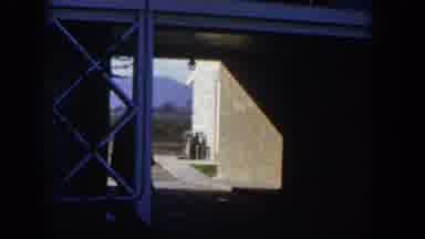 Nevada (1954): Person Wearing Hat And Glasses Walks Past White Trellis On A Sunny