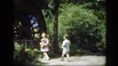 Washington DC (1948): Two Kids Stand Near Brown Wooden Water Wheel On A Sunny Day