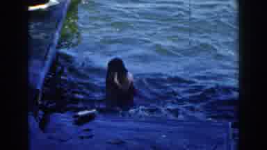 Brighton Michigan (1960): A Woman Swims In Water As Some Others Sail On A Canoe