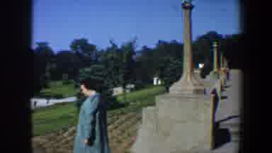 Saint Louis Missouri (1964): Woman Wearing Blue Coat Walks Past Small Green Bush