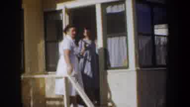 Wyoming (1957): Woman Wearing White Sweater Carries Tan Box To Blue Car On A Sunny