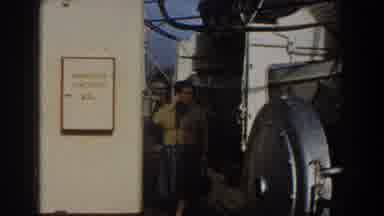 Gibraltar (1959): Woman Wearing Yellow Sweater Stands Near Large Grey Object On A