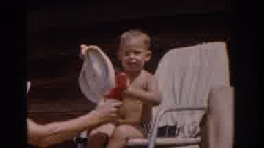 Van Nuys California (1962): Small Boy Sitting In White Chair Tries To Put On White