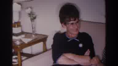 Madison Wisconsin (1966): Woman Wearing Blue Dress And Glasses Sits On Tan Sofa