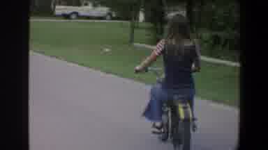 Minnesota (1973): Girl Riding A Motorcycle In A Street Near Other House