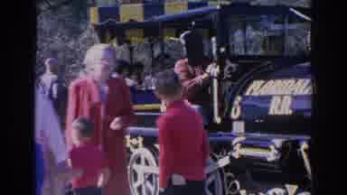 Sarasota Florida (1969): Woman Wearing Red Coat Looks At Blue And Yellow Train