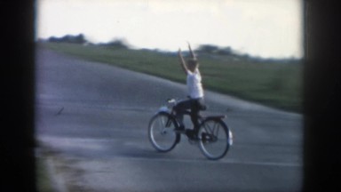 1958: Woman Riding A Bike Down A Street