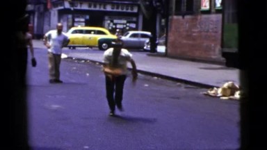1956: A Man Riding A Skateboard Down A Street.