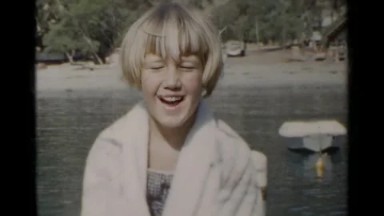 1955: Young Girl Smiling and Sitting on a Boat Near a Lake
