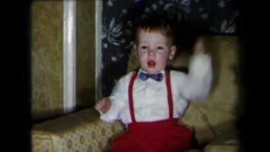 1971: Young Boy in White Shirt and Blue Bowtie Sitting and Holding Phone