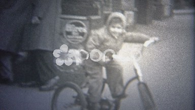 1946: Boy riding bike on streets past a local urban news-stand.