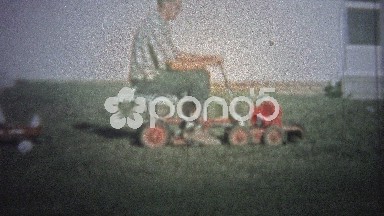 NEW HAVEN, CONN. USA - 1957: Dad on new riding lawn mower towing kids on back.