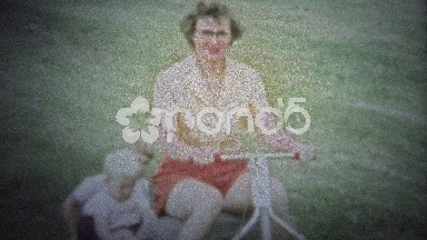 NEW HAVEN, CONN. USA - 1957: Mom on new riding lawn mower towing kids on back.
