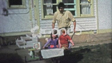 BOULDER, CO. USA - 1974: Dad pushing kids around the yard in a wheelbarrow.