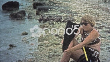 1973: Women putting on snorkeling gear and swimming into the waves.