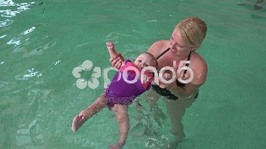 Mom teaching lifejacket baby to swim.