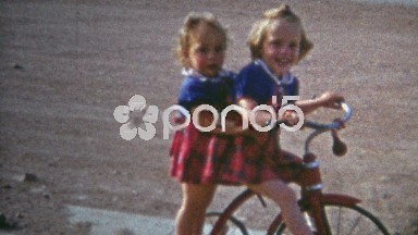 Boulder, Colorado (1952): Sisters riding tricycle suburban sidewalk street.