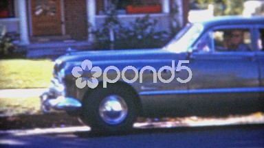 1953: Family driving off in new car into the suburban-scape.