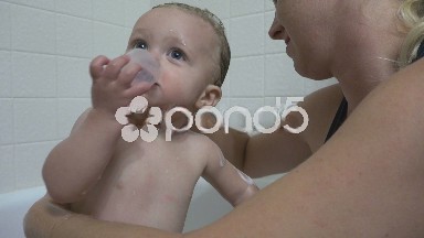Mom washing baby bath time while she eats something.