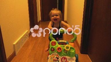 Baby learning to stand using toy walker chase down hall.