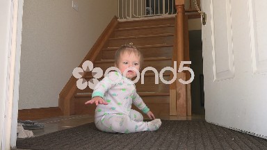 Baby thinking about steps near open front door.