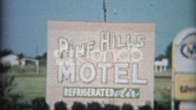 1957: Pine Hills Motel enterance sign and motor lodge with old cars.