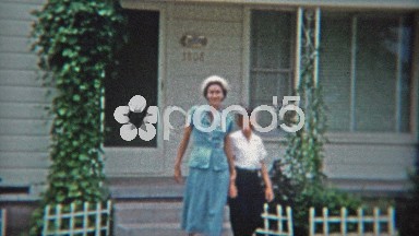1953: Mom baby blue dress with son walking past car with neighborhood pan.