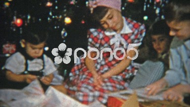 1951: Kids opening Christmas gifts in front of festive tree.
