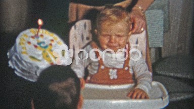 1961: Big 1st birthday cake for boy wearing suspenders in high chair.